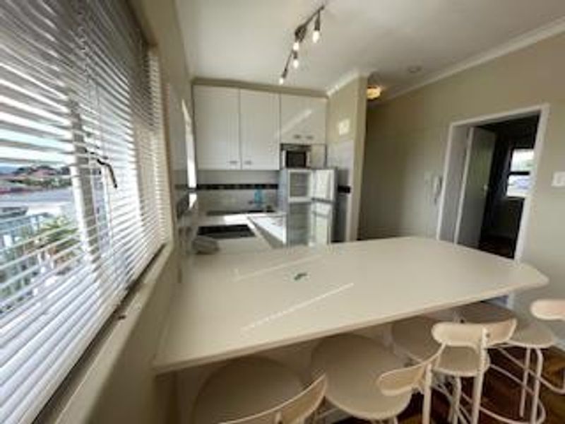 A functional kitchen featuring white cabinetry, a breakfast bar, and integrated appliances, offering a practical layout with natural light from the adjacent window.