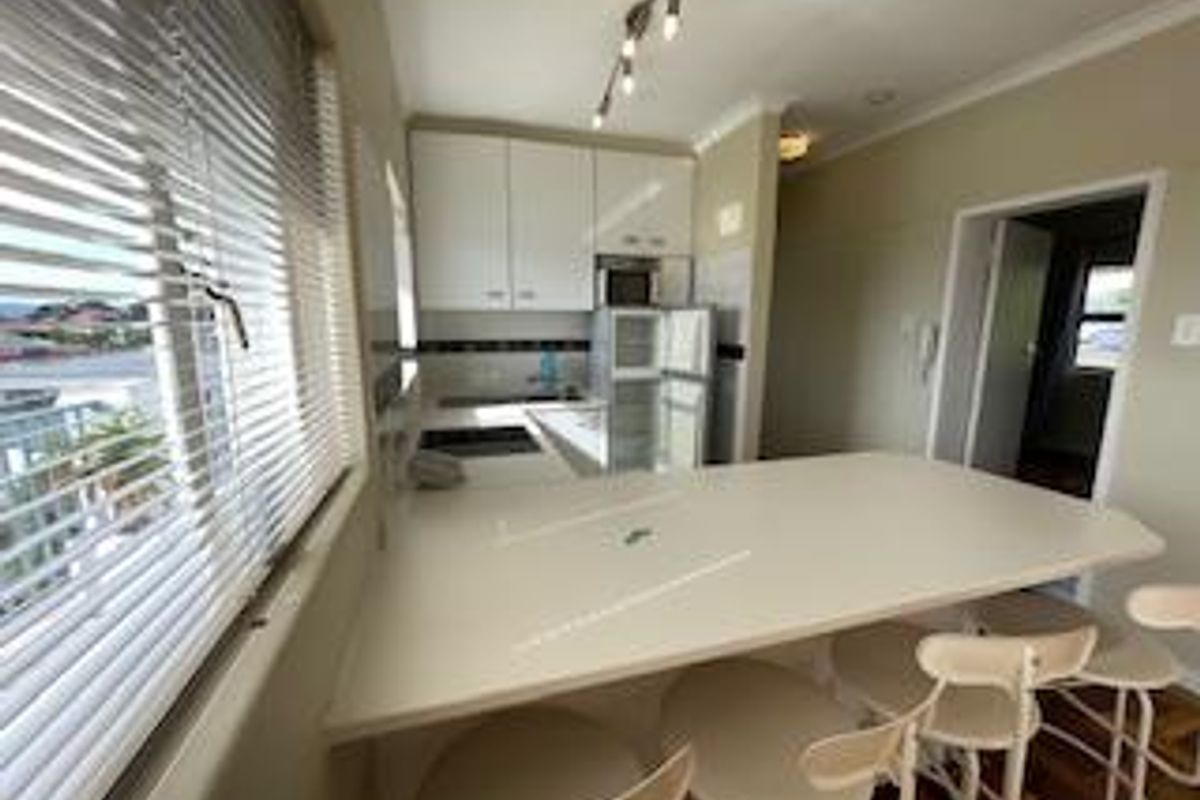 A functional kitchen featuring white cabinetry, a breakfast bar, and integrated appliances, offering a practical layout with natural light from the adjacent window.
