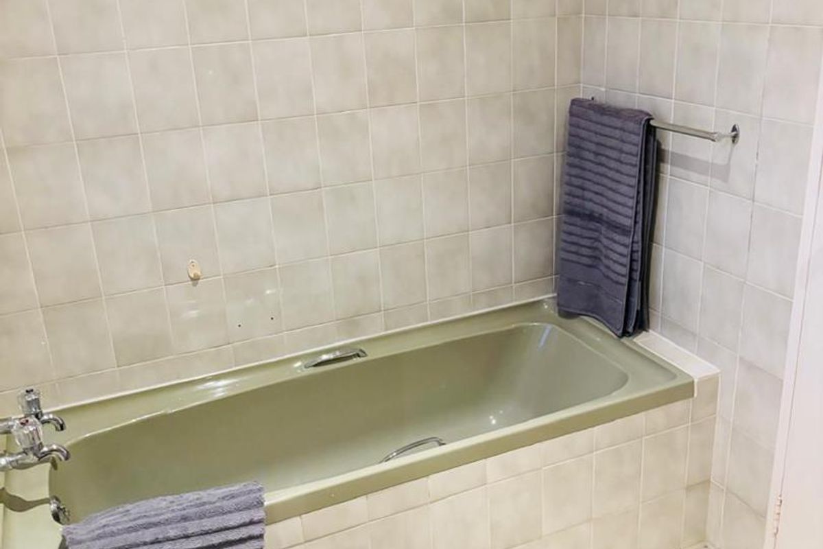 A dated bathroom featuring a built-in bathtub with light-colored wall tiles and a matching basin.