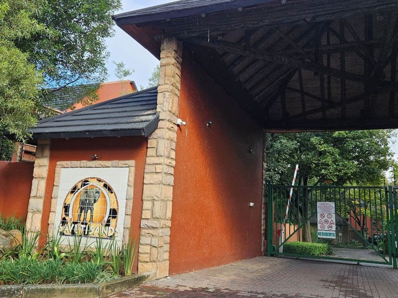 The entrance to the apartment complex features a secure gated access point with stone-clad pillars and a covered guardhouse structure.