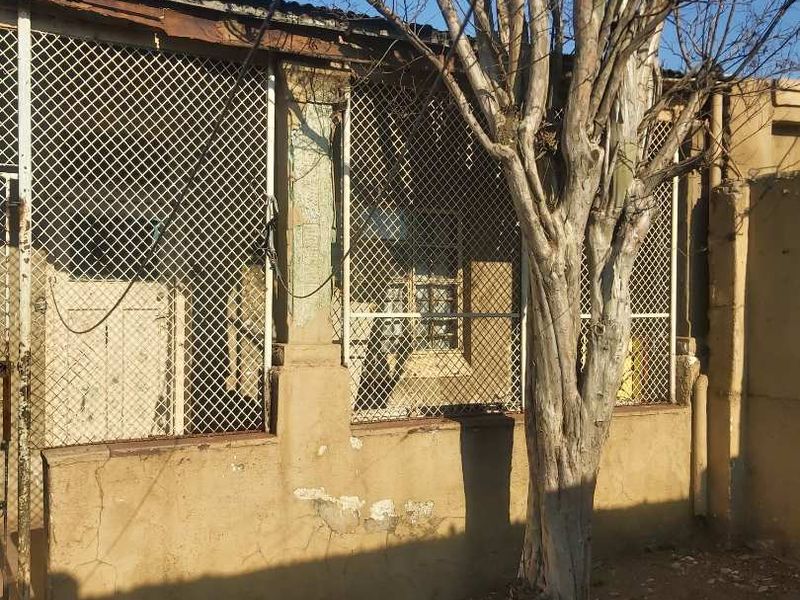Rear exterior view of the property showing a masonry wall with security mesh fencing and signs of significant structural wear and weathering.