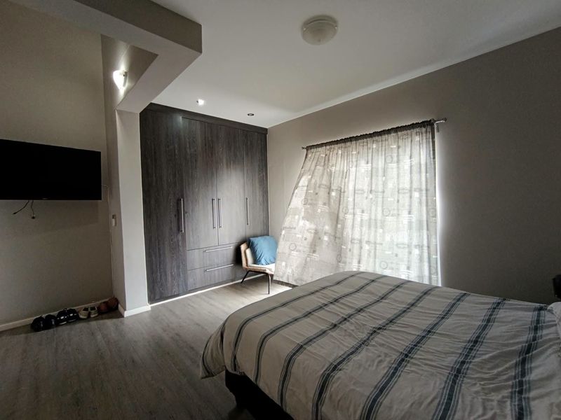 A well-maintained bedroom featuring dark wood built-in cupboards, modern laminate flooring, and neutral wall tones, providing a functional and comfortable living space.