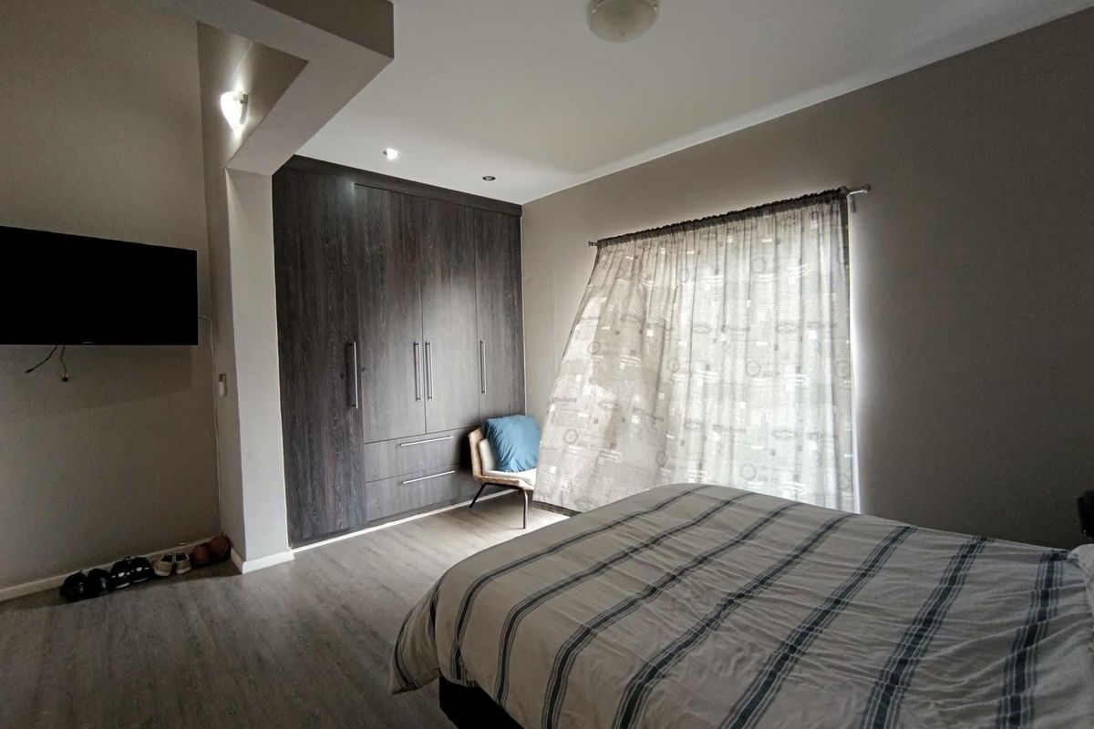 A well-maintained bedroom featuring dark wood built-in cupboards, modern laminate flooring, and neutral wall tones, providing a functional and comfortable living space.