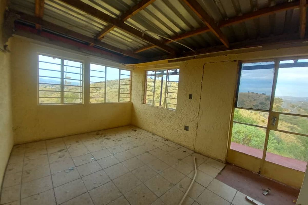 An empty, unfinished room featuring tiled flooring, large windows with scenic views, and an exposed timber and corrugated metal roof structure.