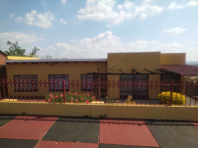 Front exterior view of a single-story house featuring a tiled driveway, metal security fencing, and a timber pergola over the entrance area.