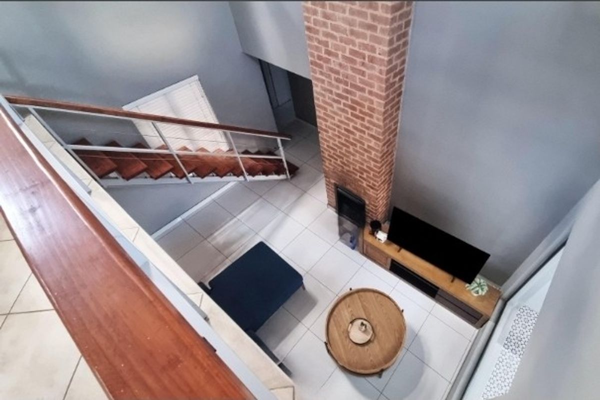 A high-angle view of a living area featuring an exposed brick chimney breast, a built-in fireplace, and a staircase with wooden treads.