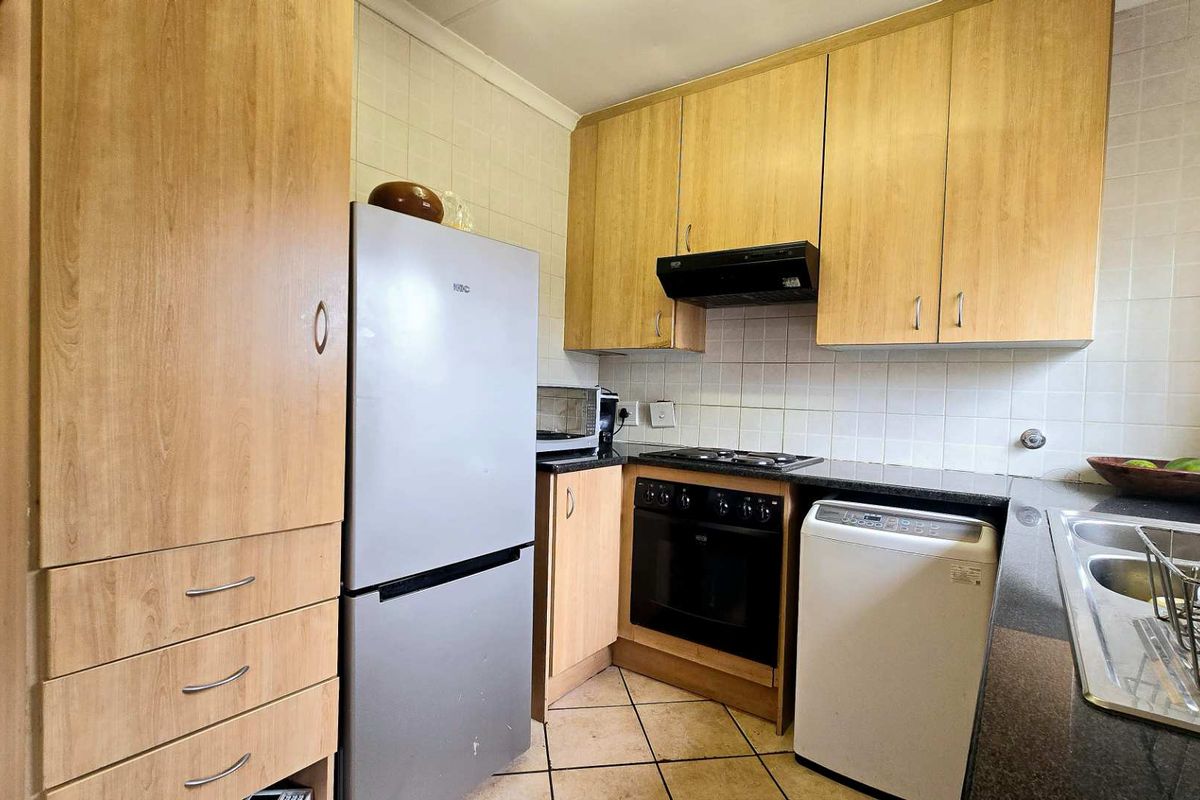 Functional kitchen featuring light wood-finish cabinetry, dark granite countertops, built-in oven, gas hob, extractor fan, and a double-basin stainless steel sink.
