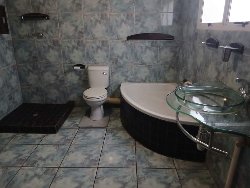 Bathroom featuring a corner bathtub, walk-in shower base, toilet, and glass vessel sink with blue patterned wall and floor tiles.