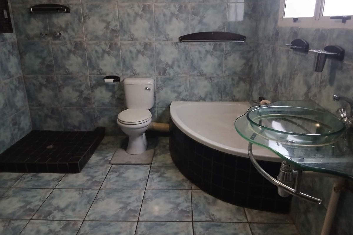 Bathroom featuring a corner bathtub, walk-in shower base, toilet, and glass vessel sink with blue patterned wall and floor tiles.