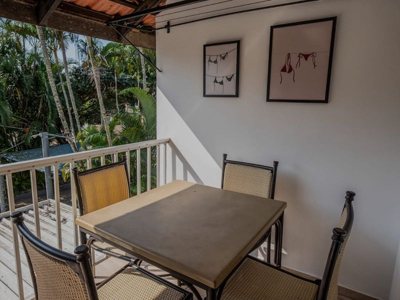 A covered balcony area featuring a railing and exposed timber roof structure, overlooking lush greenery.