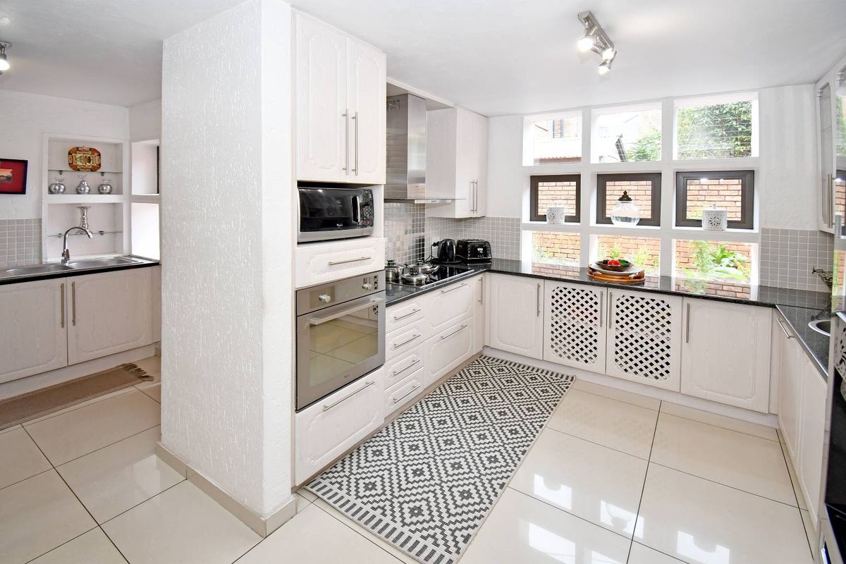 A bright, well-maintained kitchen featuring white cabinetry, dark granite countertops, built-in oven, hob, extractor fan, and a separate scullery area with a sink.