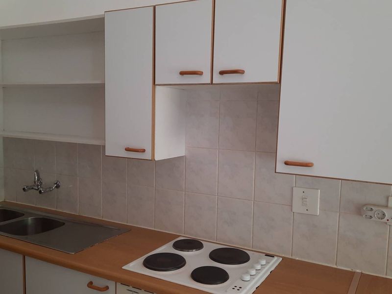 A functional kitchen featuring white cabinetry, laminate countertops, a double stainless steel sink, and a built-in electric hob with tiled backsplash.