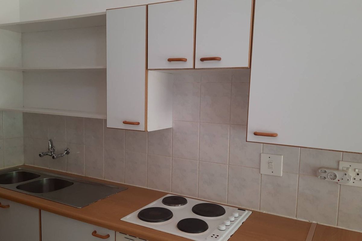 A functional kitchen featuring white cabinetry, laminate countertops, a double stainless steel sink, and a built-in electric hob with tiled backsplash.