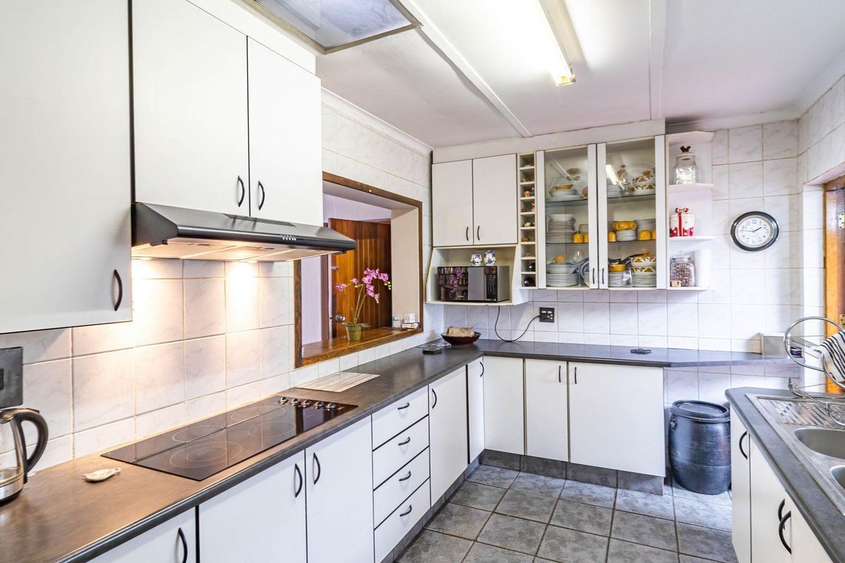 Functional kitchen featuring white cabinetry, dark laminate countertops, a built-in electric hob, extractor fan, and tiled splashbacks with a convenient serving hatch.