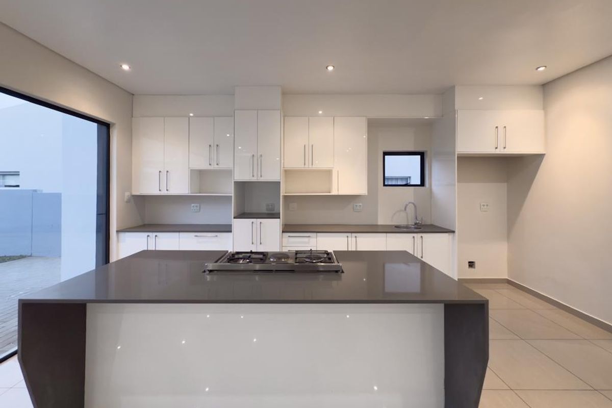 Modern kitchen featuring white cabinetry, stone countertops, a central island with a built-in gas hob, and large format floor tiles.