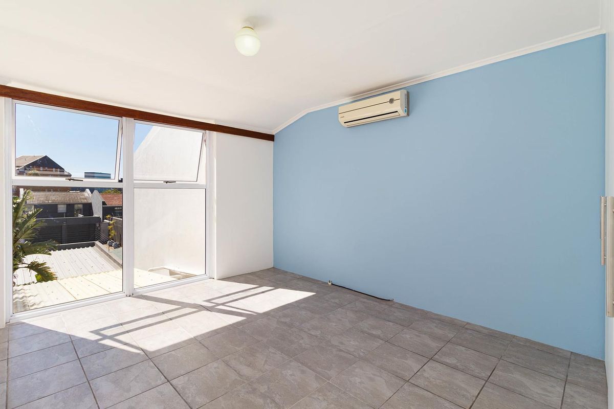 An empty bedroom featuring tiled flooring, a wall-mounted split-system air conditioner, and large windows providing natural light.