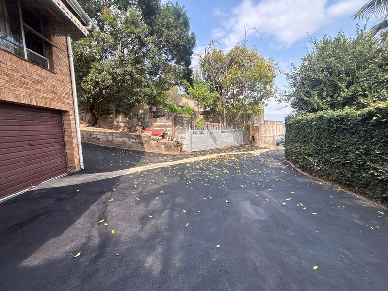 A paved driveway leading to a brick-faced garage, featuring a retaining wall and established garden hedging.