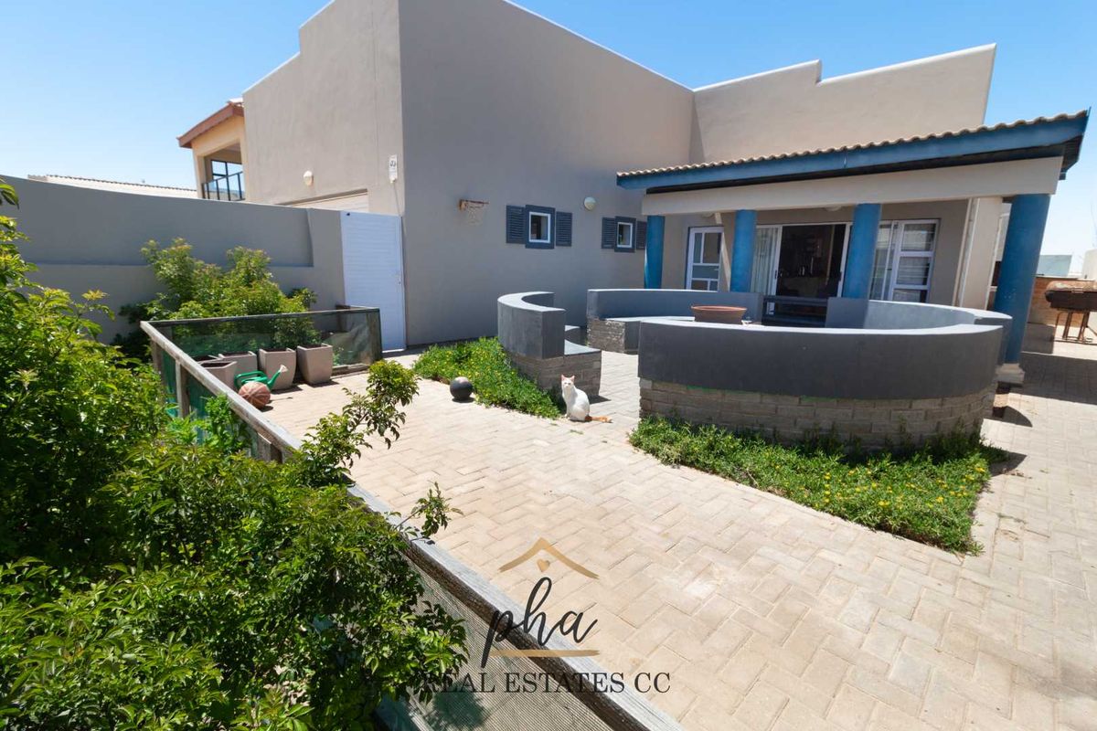 Rear exterior view featuring a paved patio area with built-in curved seating, covered veranda, and landscaped garden space.