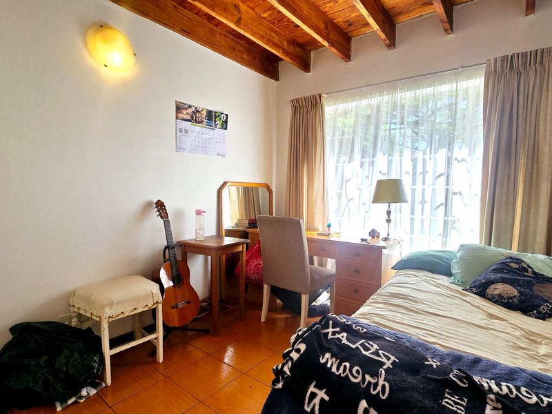 A bedroom featuring exposed timber ceiling beams, tiled flooring, and a wall-mounted light fixture, offering a cozy and rustic atmosphere.