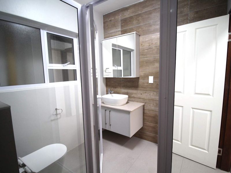 A modern, clean bathroom featuring a wall-mounted vanity with a vessel sink, a mirrored medicine cabinet, and a tiled feature wall.