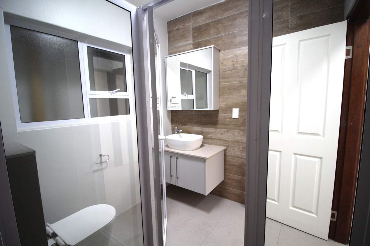 A modern, clean bathroom featuring a wall-mounted vanity with a vessel sink, a mirrored medicine cabinet, and a tiled feature wall.