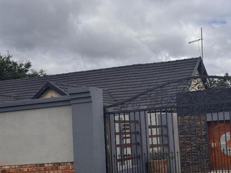 Front view of the property featuring a tiled roof, secure perimeter wall with wrought iron gate, and decorative stone cladding at the entrance.