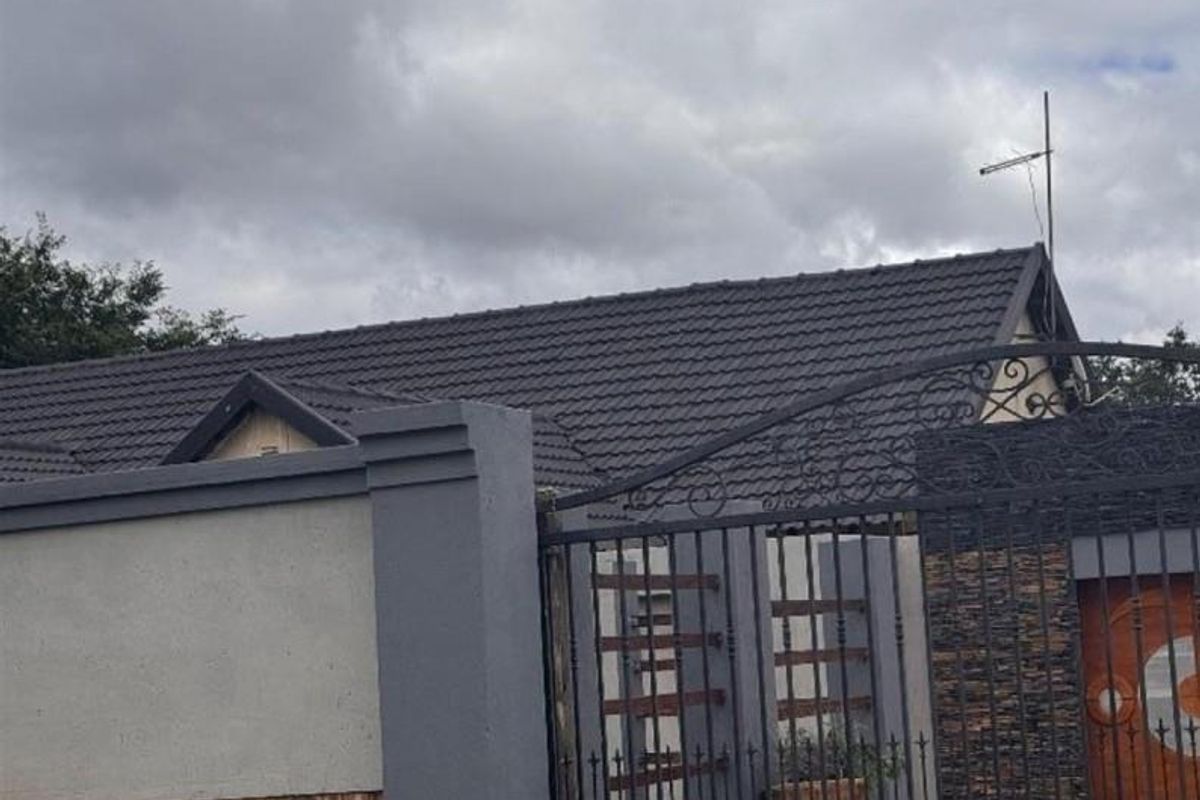 Front view of the property featuring a tiled roof, secure perimeter wall with wrought iron gate, and decorative stone cladding at the entrance.