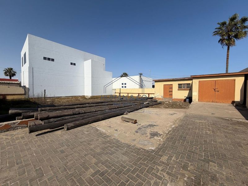 Rear exterior view of the property featuring a paved driveway, garage access, and surrounding boundary walls with open yard space.
