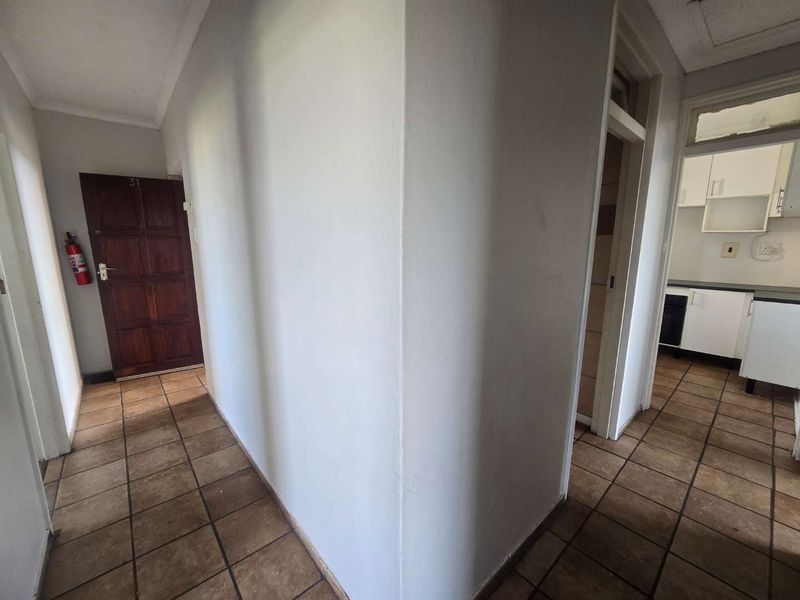 A functional apartment hallway with tiled flooring, leading to the main entrance and an adjacent kitchen area.
