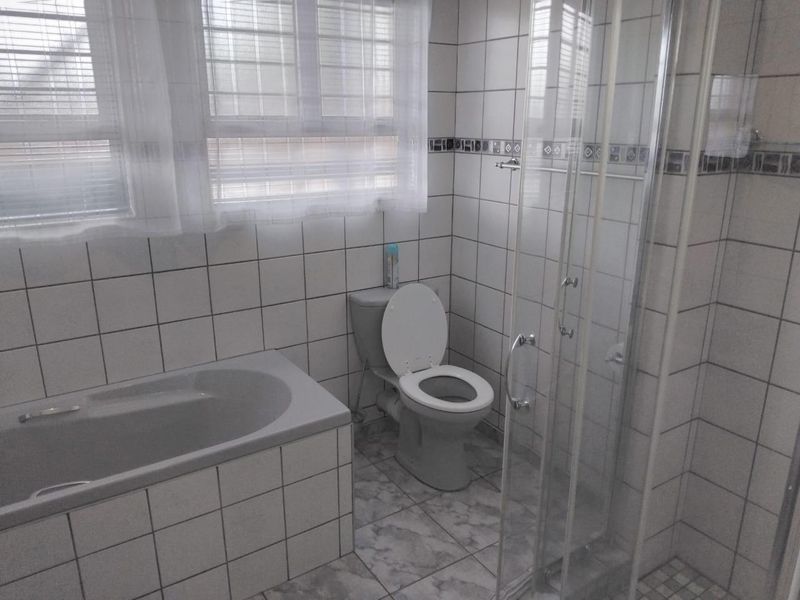 A functional bathroom featuring a built-in bathtub, a separate glass-enclosed shower, and tiled finishes throughout.