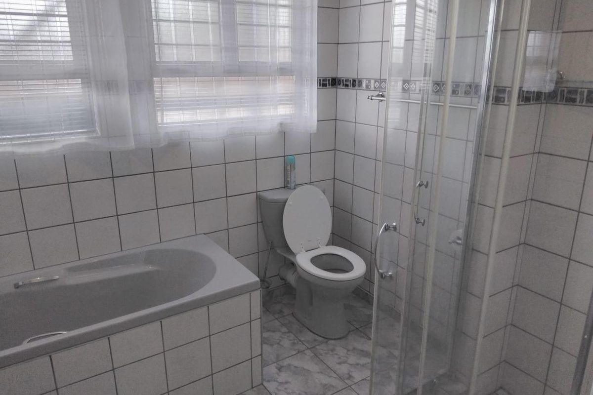 A functional bathroom featuring a built-in bathtub, a separate glass-enclosed shower, and tiled finishes throughout.