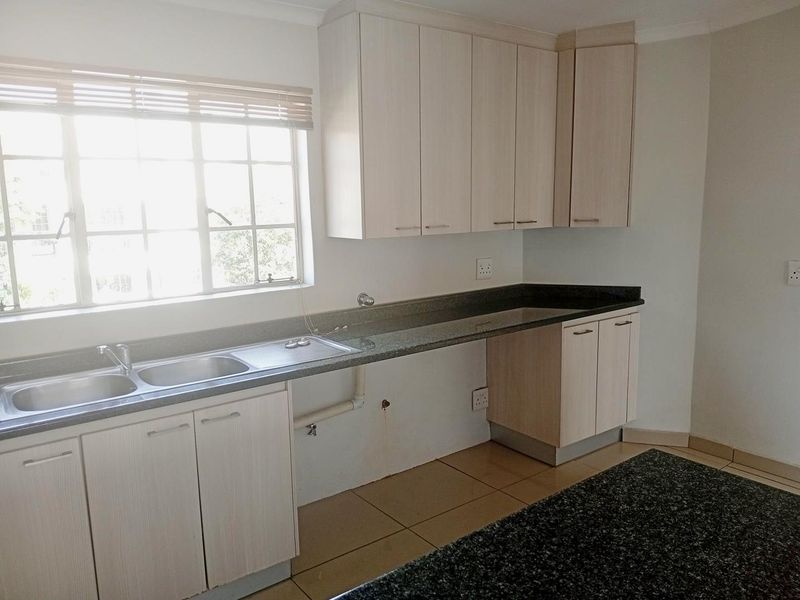 A functional kitchen featuring light wood cabinetry, granite countertops, a double basin sink, and tiled flooring, offering a clean and neutral space.