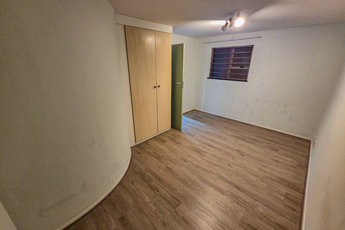 An empty bedroom featuring laminate flooring, a built-in wardrobe, and a louver window. The walls show signs of wear and require cosmetic attention.