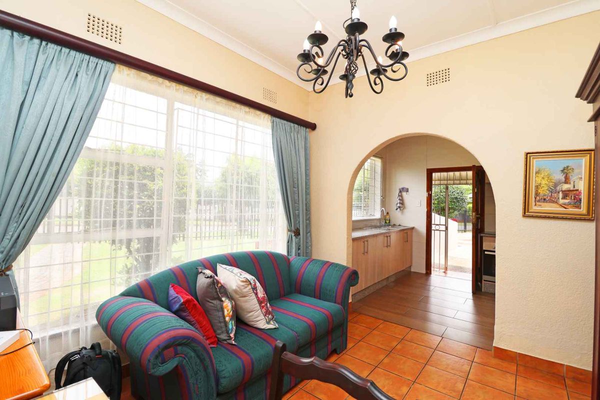 A living area featuring tiled flooring, an arched doorway leading to a kitchen space, and large windows with natural light.