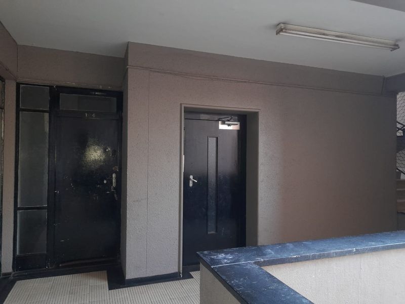 A communal apartment hallway featuring tiled flooring, security doors, and a basic overhead light fixture.