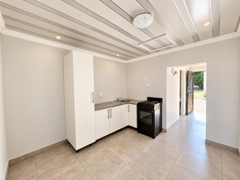 A clean, modern kitchen featuring white cabinetry, a stainless steel sink, and a freestanding stove, with tiled flooring and decorative ceiling panels.