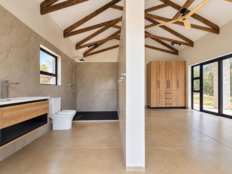 Spacious modern bathroom featuring exposed timber trusses, a walk-in shower, floating vanity, and built-in cabinetry with a clean, contemporary aesthetic.