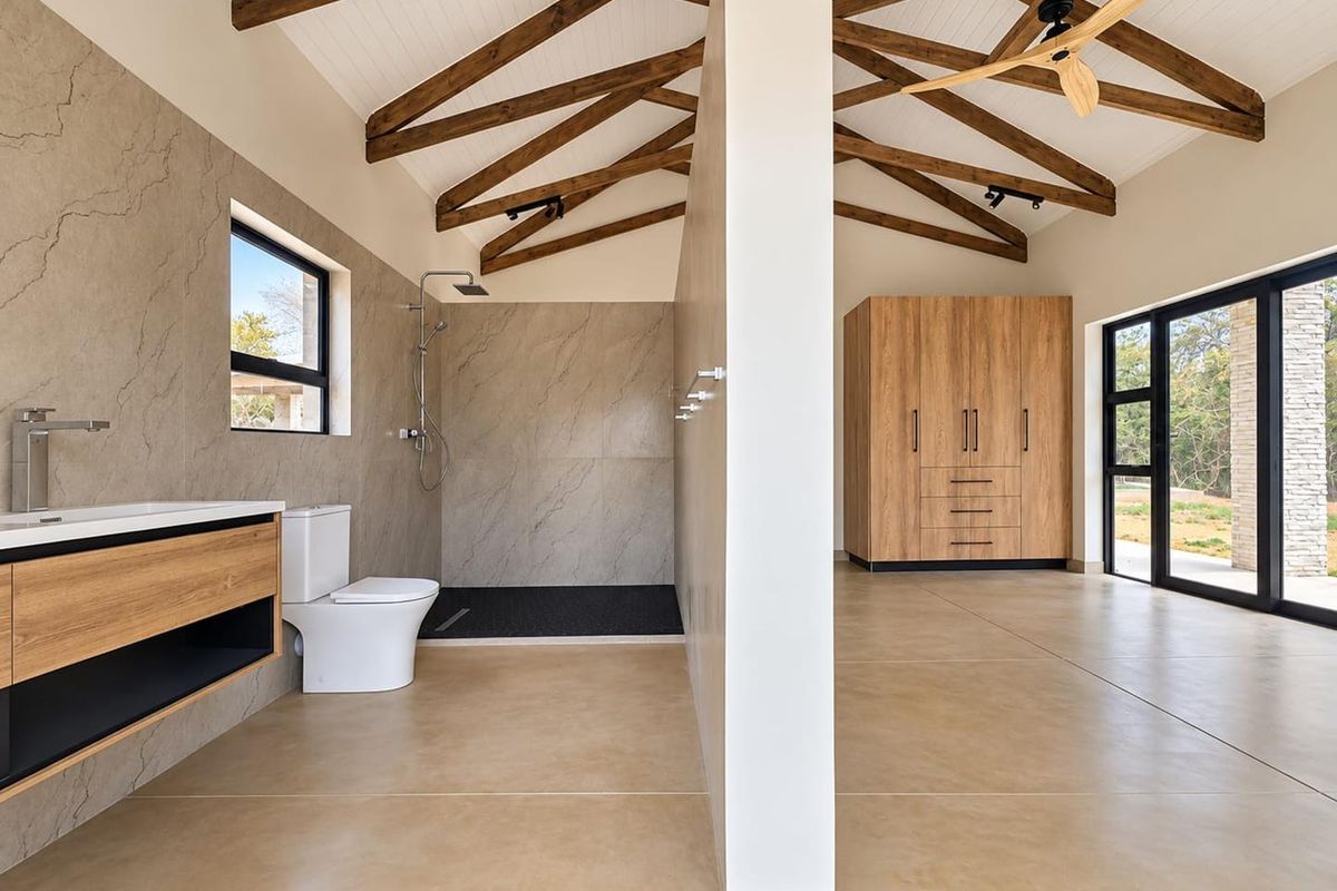 Spacious modern bathroom featuring exposed timber trusses, a walk-in shower, floating vanity, and built-in cabinetry with a clean, contemporary aesthetic.