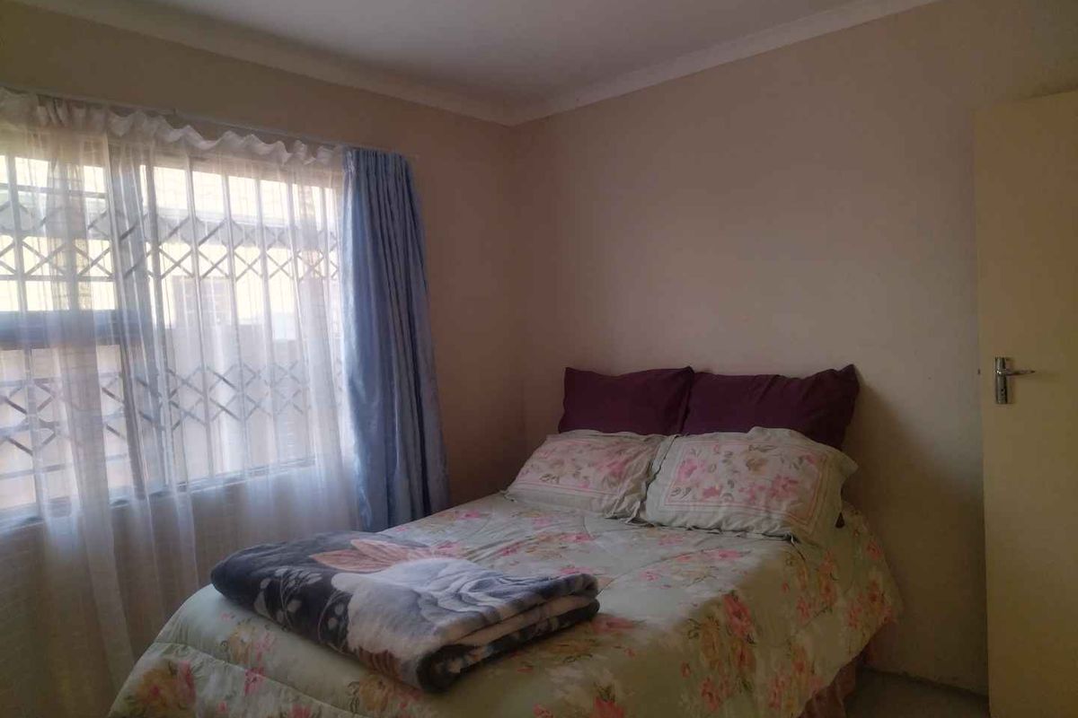 A standard bedroom featuring neutral wall finishes and a window fitted with security bars.