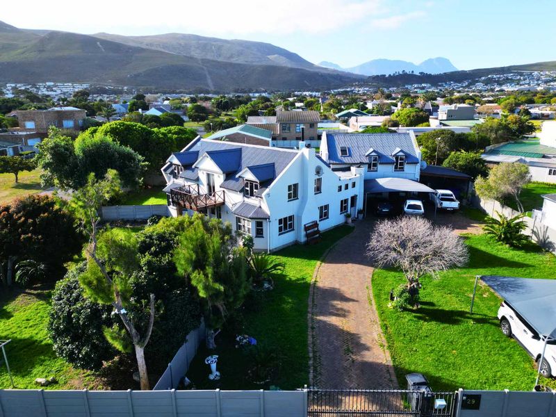 Aerial view of a large residential property featuring a multi-level home with a metal roof, paved driveway, carport, and landscaped garden.