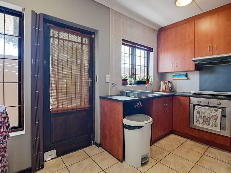 A functional kitchen featuring wood-finish cabinetry, tiled flooring, built-in oven with extractor fan, and direct access to the exterior via a security gate.