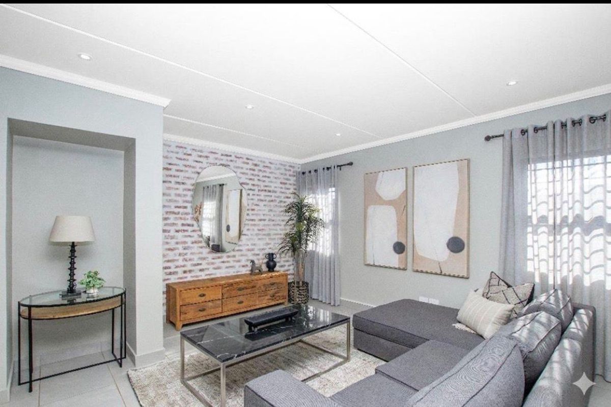 A well-maintained living room featuring a decorative brick-style accent wall, recessed ceiling lighting, and neutral tiled flooring.