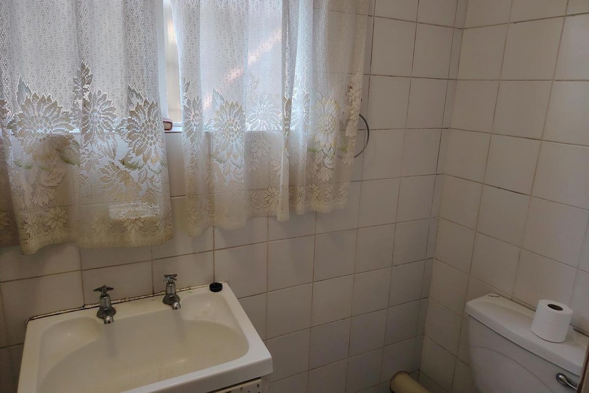 A compact bathroom featuring white ceramic wall tiles, a pedestal basin, and a standard toilet, requiring cosmetic updates to modernize the space.