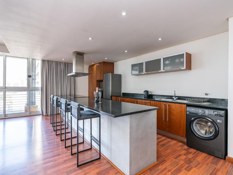 Modern open-plan kitchen featuring granite countertops, wood cabinetry, stainless steel extractor fan, and integrated laundry appliance space.