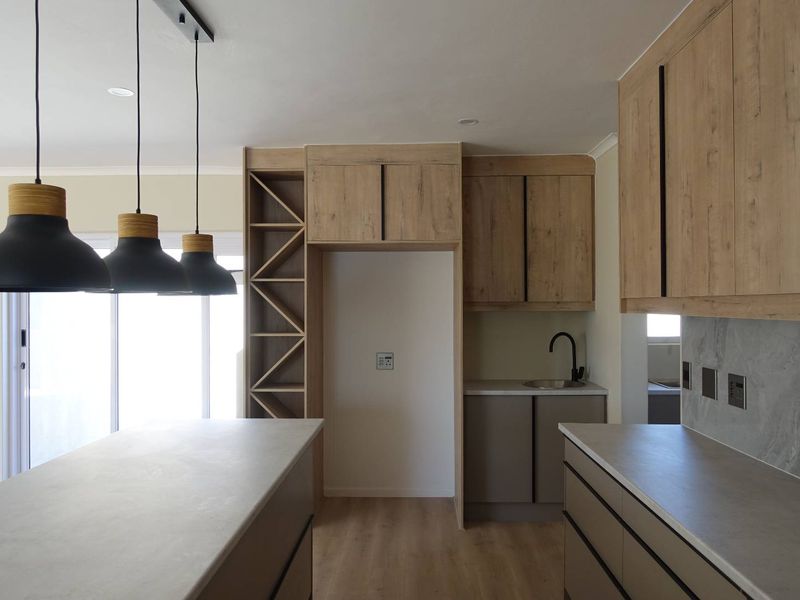 Modern kitchen featuring light wood-tone cabinetry, stone countertops, a central island, and contemporary black pendant lighting in a clean, open-plan layout.