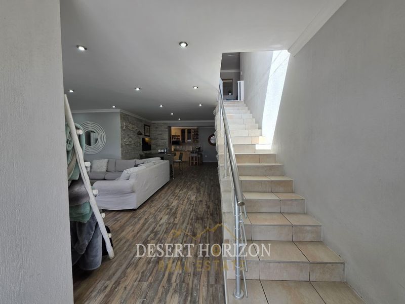 Open plan living area featuring laminate flooring, recessed lighting, a stone feature wall, and a tiled staircase with a modern metal balustrade.