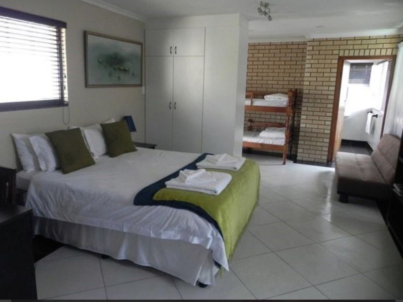 Spacious bedroom featuring tiled flooring, built-in cupboards, and an exposed brick feature wall, offering a functional layout with additional sleeping space.