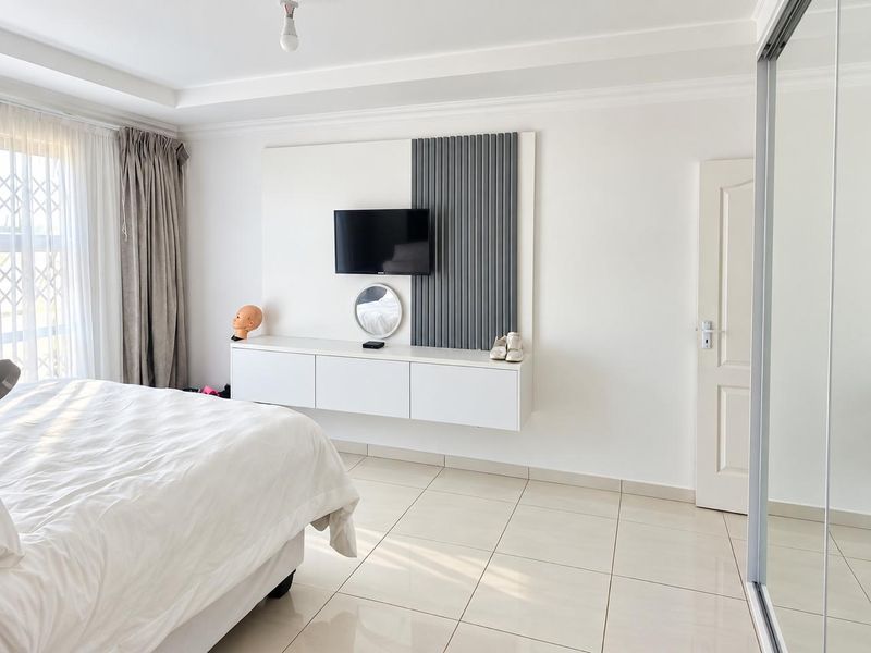 A bright bedroom featuring tiled flooring, a modern floating media console with decorative slatted wall paneling, and a built-in sliding door wardrobe.