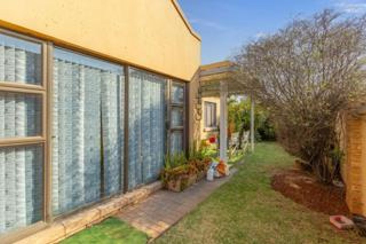 Rear exterior view of the property featuring a paved walkway, sliding glass doors, and a small covered patio area overlooking the garden.