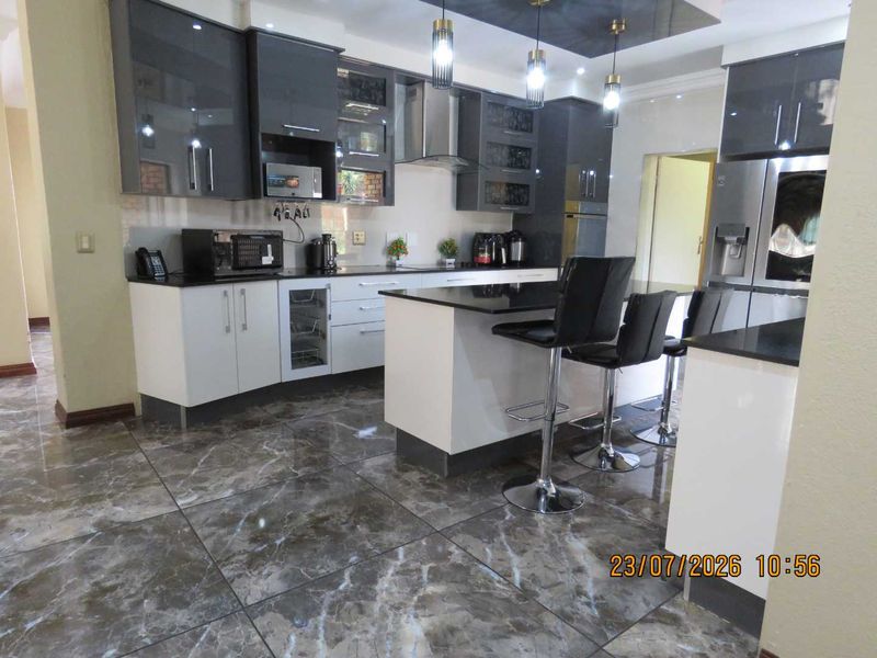 Modern kitchen featuring high-gloss cabinetry, granite countertops, a central island with breakfast bar seating, and polished marble-look floor tiles.